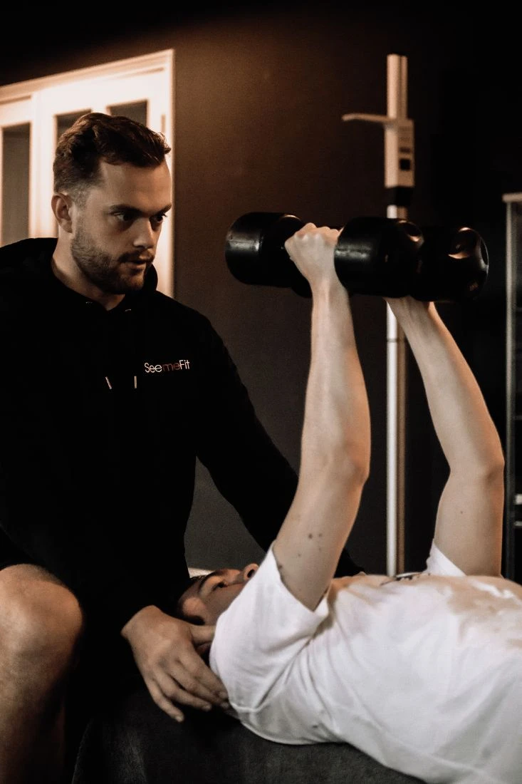 Coach kijkt mee bij dumbbell press